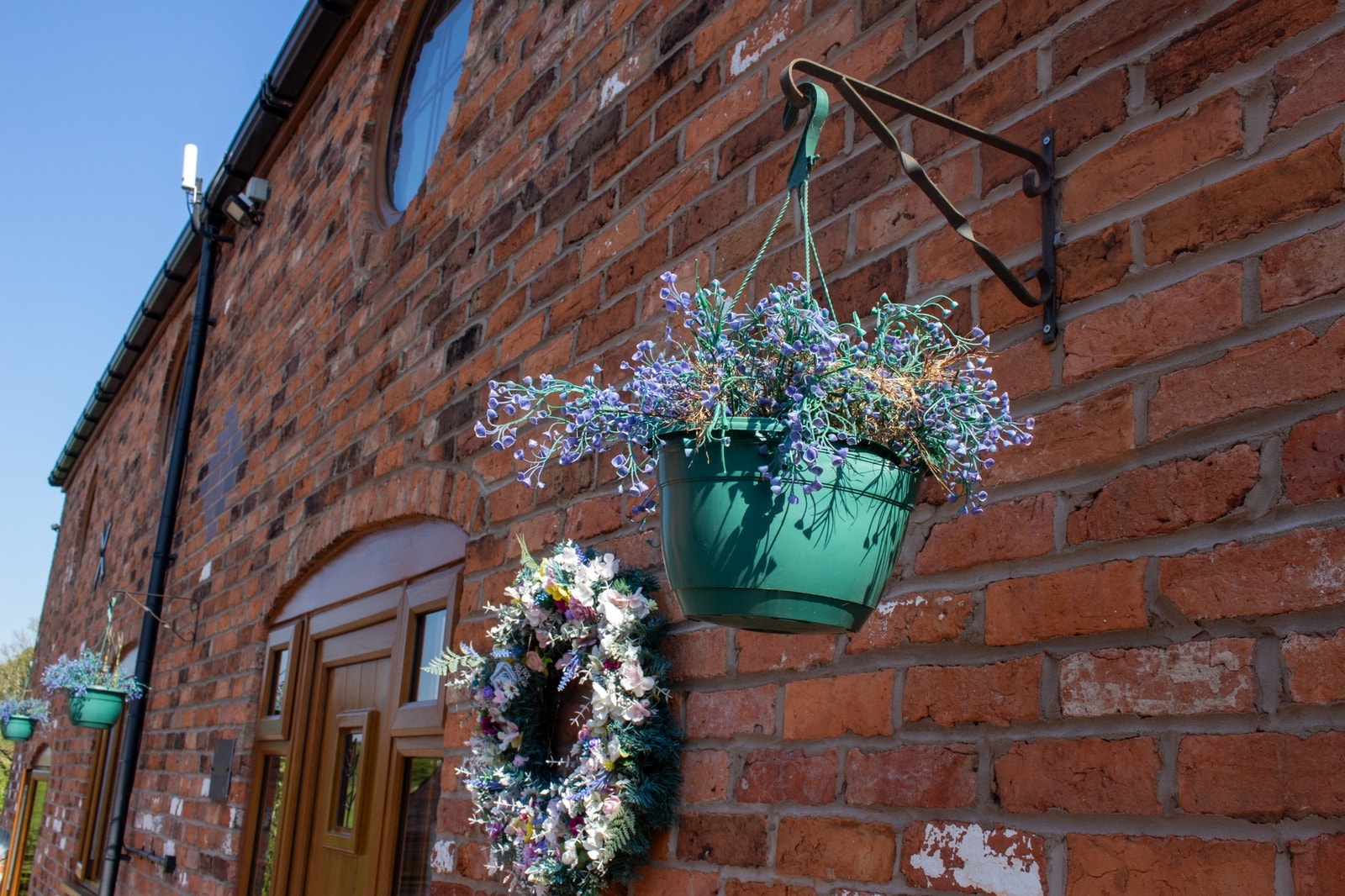 A hanging basket and a wreath beside the oak door of a converted barn